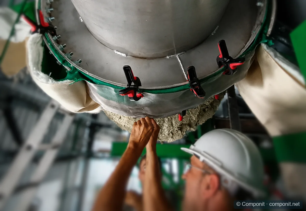 Técnicos ajustando y conformando una junta de expansión textil alrededor de un conducto industrial